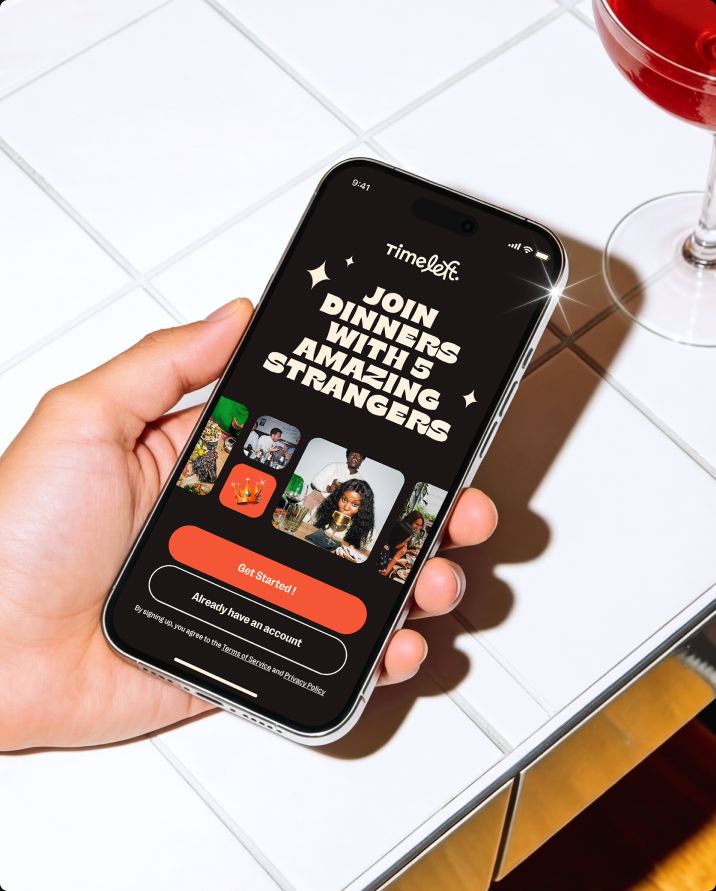 Hand holding a phone showing the Timeleft welcome screen "Join dinners with 5 amazing strangers"